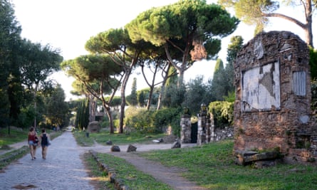 People walk past a ruined building along the tree-lined Appian Way
