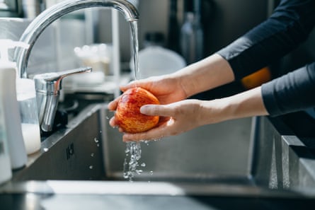 A red apple being washed under running water in a kitchen sink.
