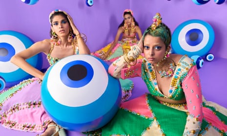 three women sit on a floor wearing bright colors amid beach balls with evil eyes on them.