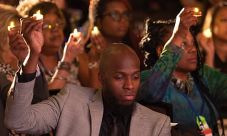 A man raises his hand while casting his eyes downward.