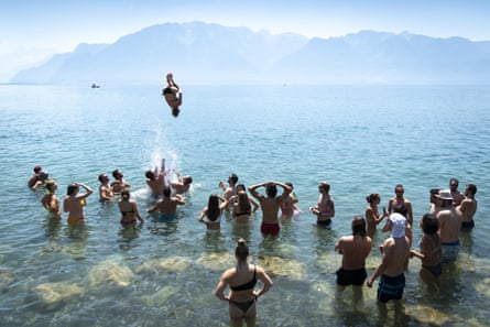 A group of people in the shallows of Lake Geneva, one doing a somersault into the water
