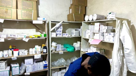A worker in a blue uniform in front of shelves full of medication.
