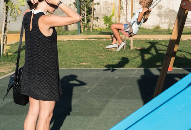 A woman standing in a playground in Spain with a child on a swing in the background