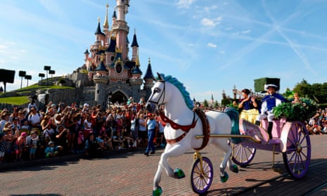 a fake horse and carriage goes past a crowd outside a pink turreted castle