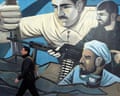 A man walks past an mural in Tehran showing men holding weapons