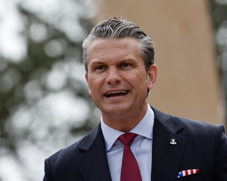 Hegseth speaks outdoors with trees and a building behind him