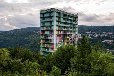 In Chiatura, Georgia, a tall weathered residential tower with colourful lower floors stands amid trees