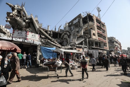 A market in Gaza among the rubble with people and man pushing shopping trolley