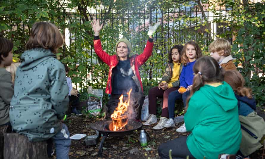 A pistillate with children gathered circular a campfire gestures with some hands