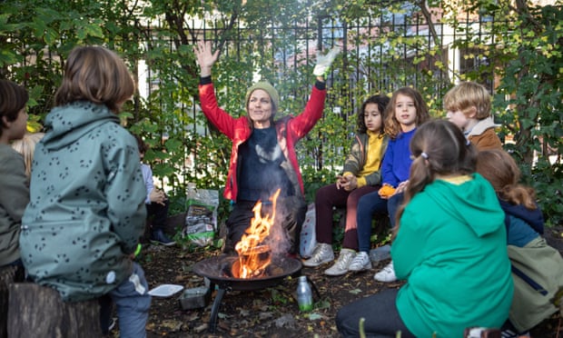 A woman with children gathered round a campfire gestures with both hands