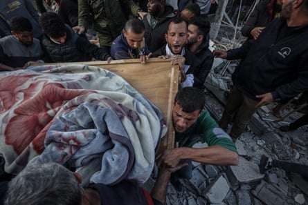 Palestinians carry a body pulled from the rubble as civil defence teams conduct search and rescue operations in the rubble of the Deir al-Balah Municipality Building after an Israeli army attack