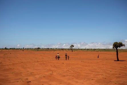 Two women walk with two small children through an expanse of red sand