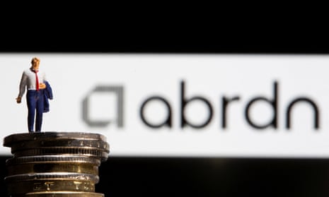 Businessman toy figure is placed on pound coins in front of displayed Abrdn logo.