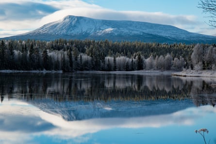 Long, low mountain, forest and reflections in a lake in western Sweden in winter.