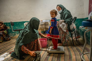 A young girl standing on weighing scales accompanied by two women