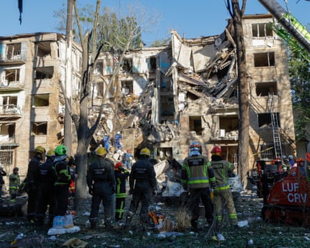 Rescue workers stand in front of badly damaged block of flats.
