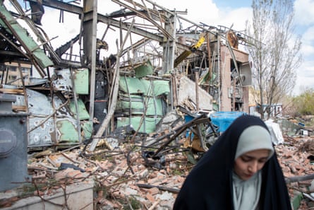 A woman walks in front of the wreckage of a building