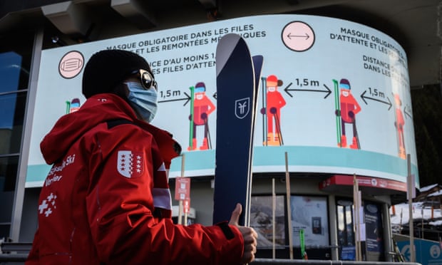 A ski instructor walks past a screen with social distancing instructions at the start of a ski lift in the Alpine resort of Verbier.