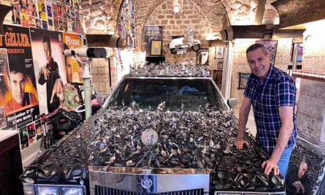 Uri Geller with 2,000 bent spoons on a Cadillac at his museum.
