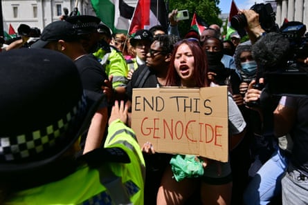 A woman holding a sign saying ‘end this genocide’ confronts police officers at a protest