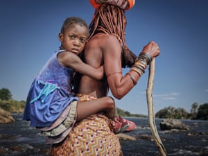 Kaevarua Tjiuma se apoia em uma bengala enquanto carrega a neta nas costas