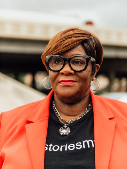 Black woman with thick glasses and an orange blazer stands for a portrait