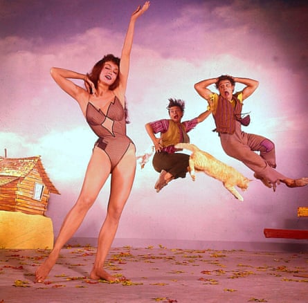 A woman performs in a skimpy bodysuit while two men animatedly jump behind her.