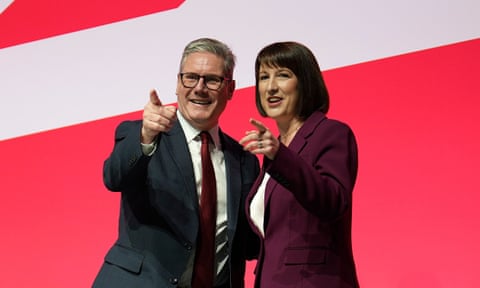They stand smiling in front of a red and white backdrop