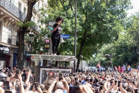 Assa Traoré on top of a bus stop, speaking into a megaphone