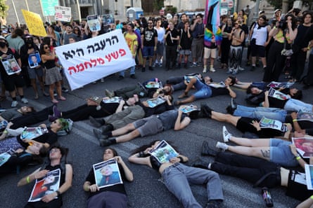 Na Parada do Orgulho LGBT em Jerusalém, em maio, as pessoas estão deitadas na rua, a maioria de jeans e shorts, segurando fotos de palestinos mortos, com outras pessoas ao seu redor, algumas segurando uma faixa com palavras em hebraico