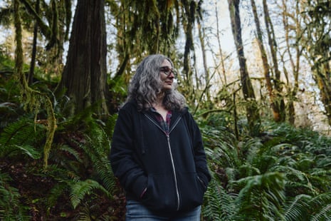 A woman in a dark hoodie stands for a portrait in a forest
