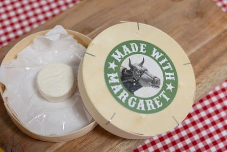 An empty box of camembert and a tiny cheese camembert on a red and white checked tablecloth