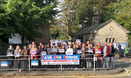 Parents demonstrate outside a school in Durham: a large group is standing on a corner in front of the gates. They have affixed a banner reading Save Our School: support our students and staff to the railings and hold placards with the same message.