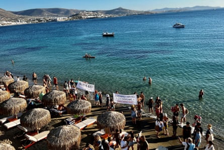 People holding banners stand on the beach at the shoreline in front of rows of sun loungers