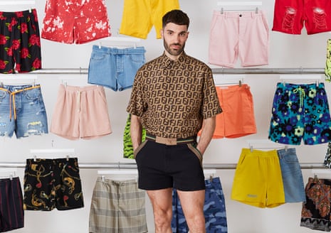 Joe Stone, wearing short shorts, in front of lots of pairs of shorts hanging up