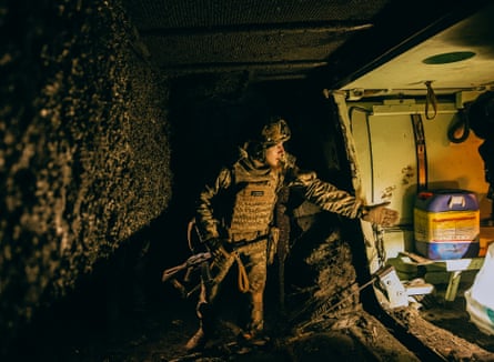 A soldier in camouflage and holding a gun loads items into a vehicle, lit only by the light from inside it