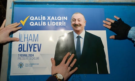 Hands hold a campaign poster of Ilham Aliyev against a wall