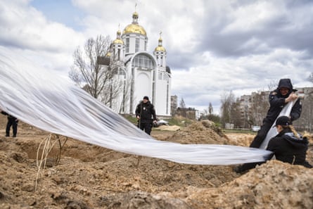 Police officers cover a mass grave in Bucha, Ukraine, in April.