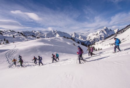 A group of people in winter clothing snowshoeing down a slope in the Austrial Alps