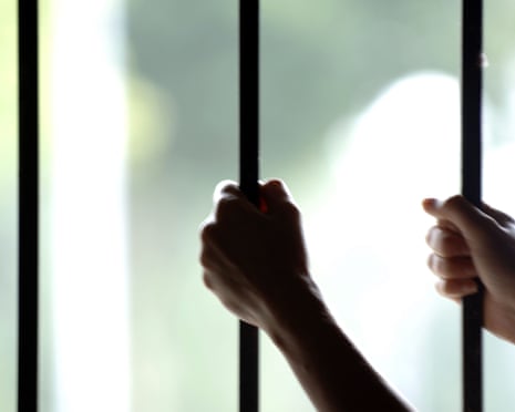 A prisoner holding on to bars in their cell