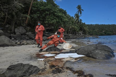 Three men in orange jumpsuits laying white pads on the water.