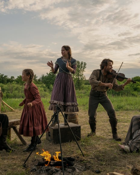 The Ingalls family, dressed in period clothing gather around a campfire in an open field in Little House on the Prairie.