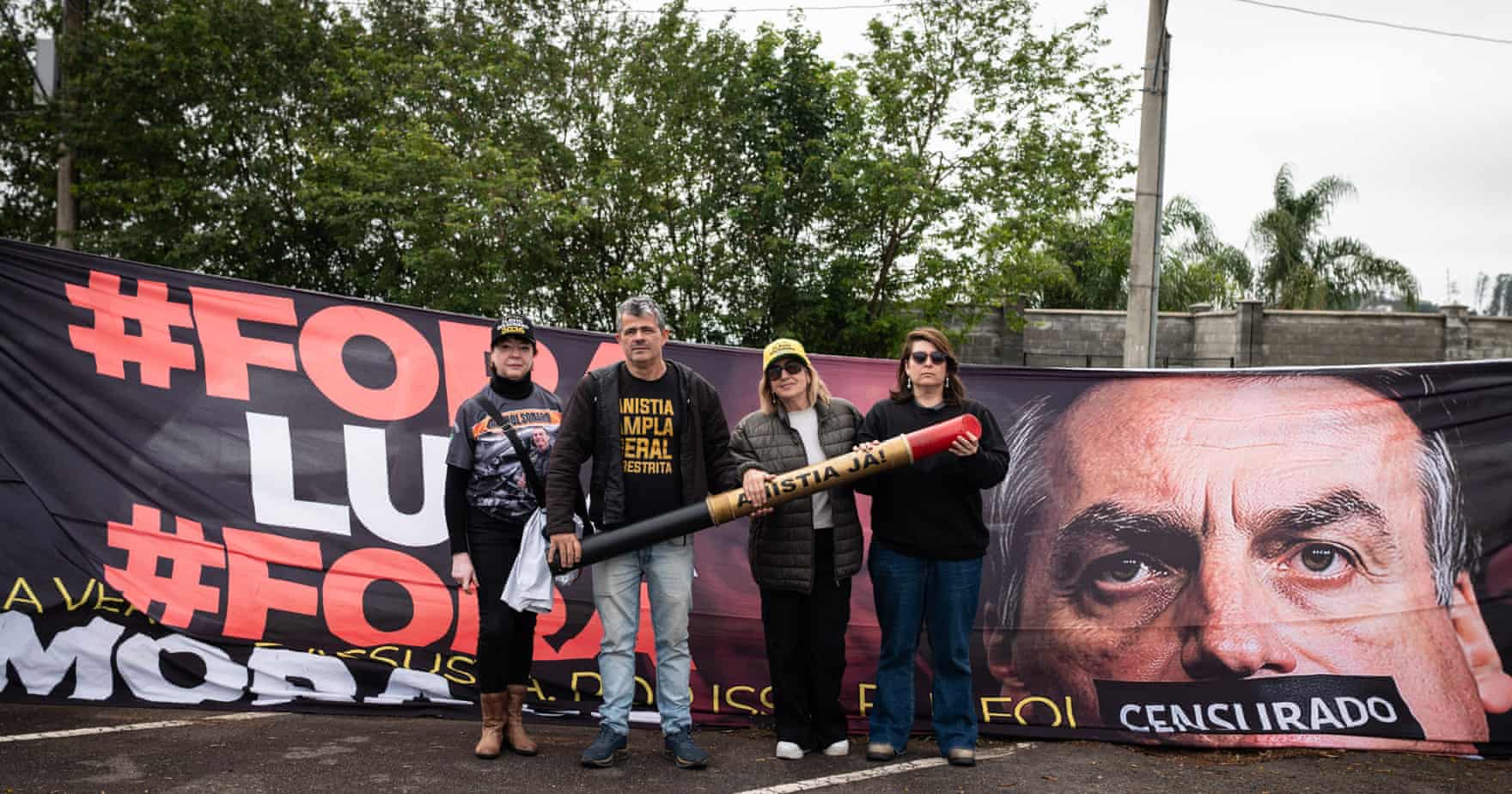 Four people stand in front of a banner featuring Jair Bolsonaro with the word “CENSURADO” across his mouth.