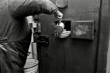 Black and white photograph of someone pouring liquid into a cup held by a prisoner through a small opening in a door.