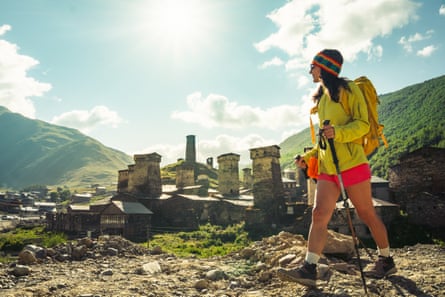Female hiker in bright clothing passes ancient looking village amid hills