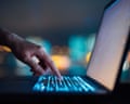 Close up of woman's hand typing on computer keyboard in the dark against colourful bokeh in background, working late on laptop at home