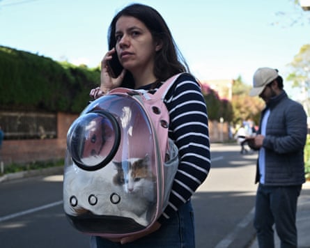 A woman with a cat in a transparent-fronted rucksack speaks on her phone