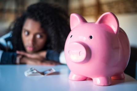 A large pink piggy bank sits on a table while a frustrated woman rests her head on her arms