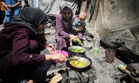 Two women, one carrying a child, cook food in a Unrwa school in Gaza