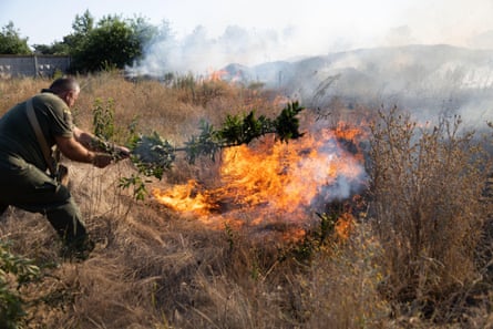 A man holds a tree branch towards a fire in the grass